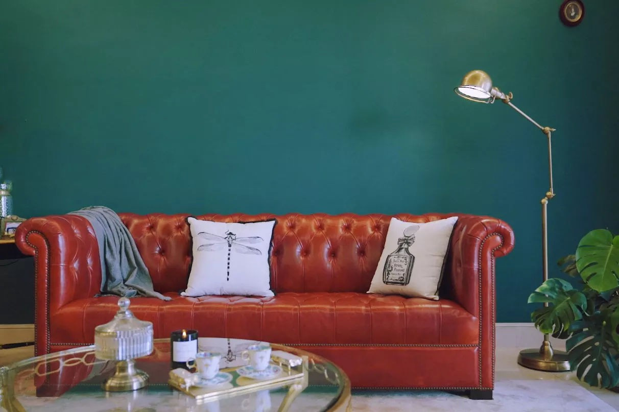 Sự kết hợp giữa sofa da đỏ và màu tường xanh đậm cùng cây đèn đứng mang nét cổ điển.